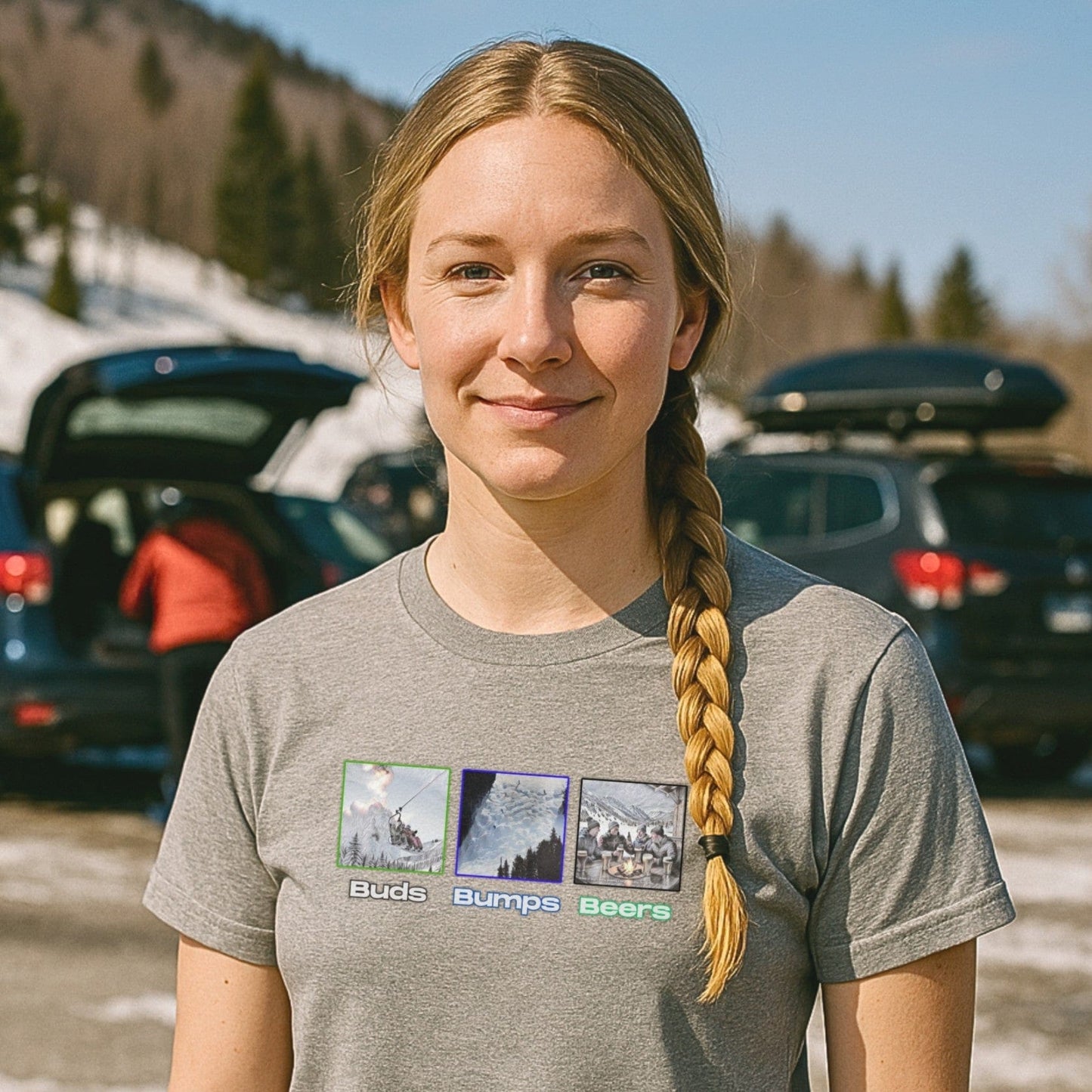 Alt Text (125 characters max):
Woman in ski parking lot wearing grey “Buds, Bumps, Beers” T-shirt with braid over shoulder, spring snow in background.