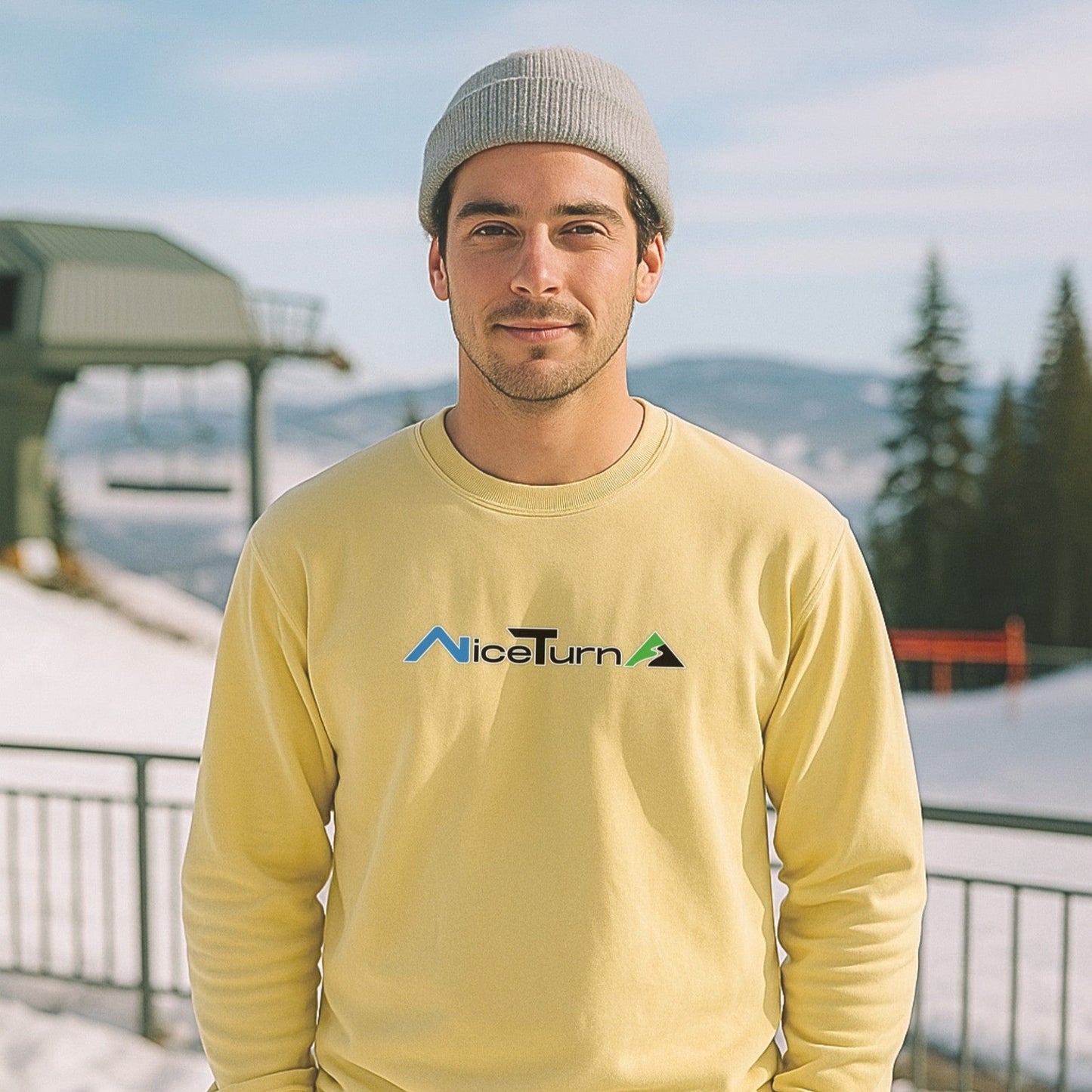 Front view of a yellow crewneck sweatshirt with the classic nice turns logo, worn by skier at a sunny lift station in the mountains.