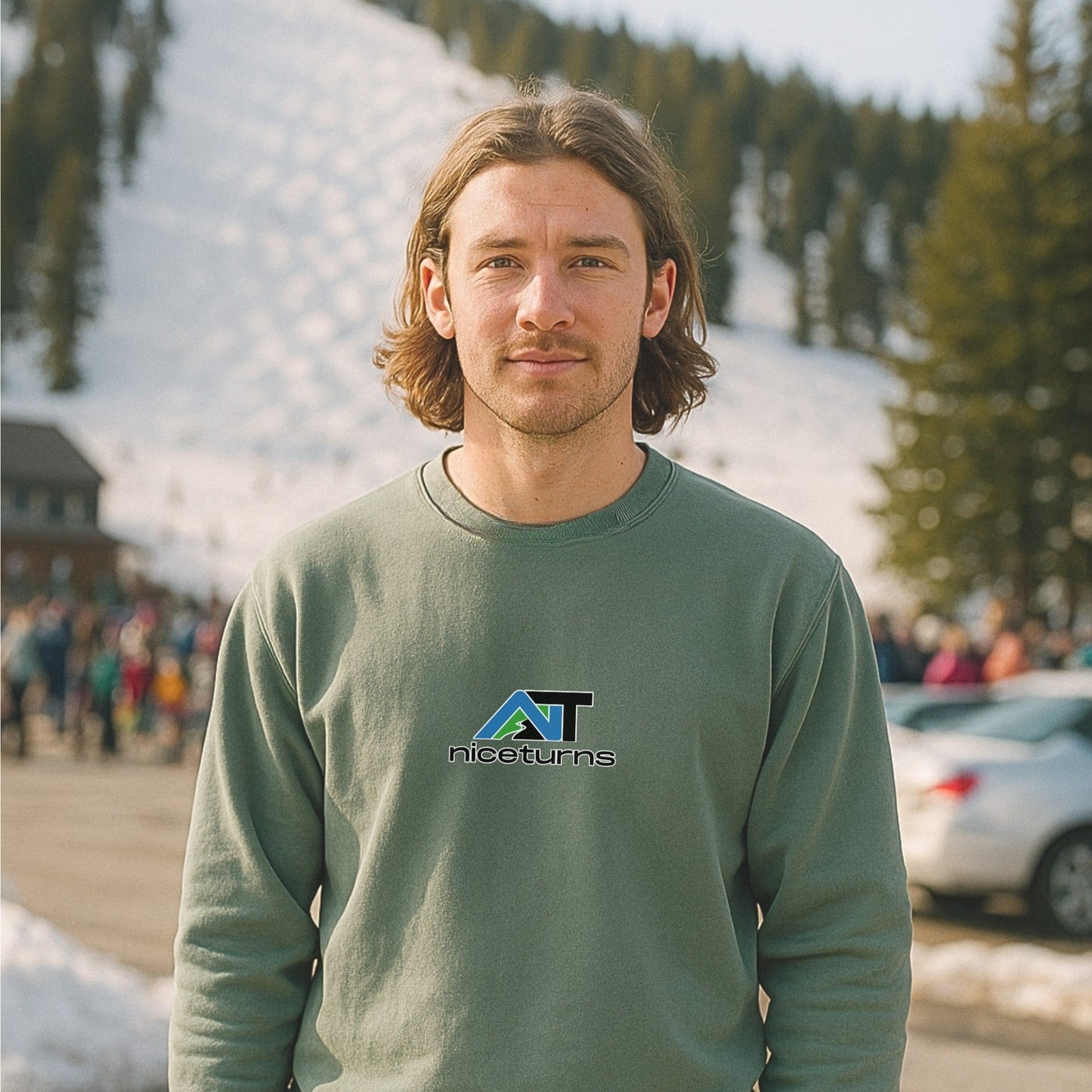 Light green crewneck sweatshirt with nice turns logo on the chest, worn in a snowy ski resort parking lot with a lift line in the background.