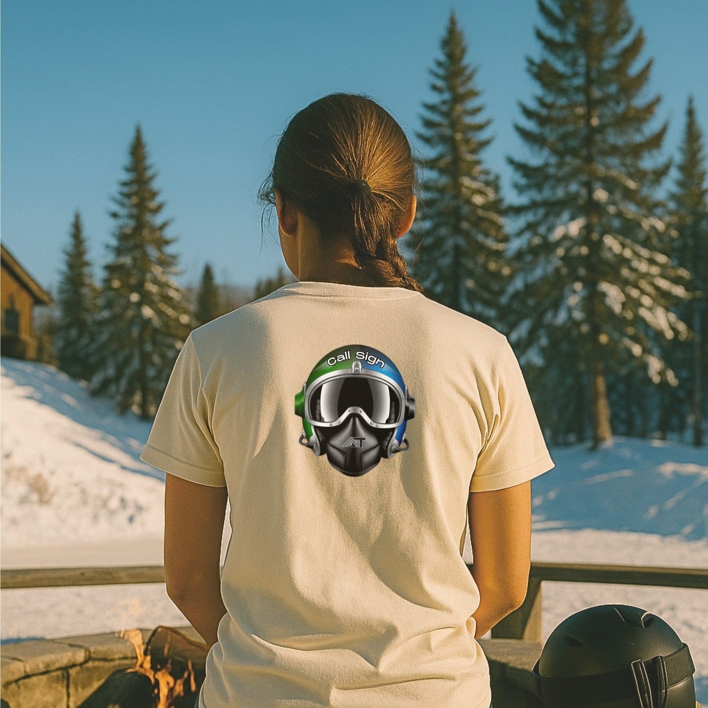 Call Sign tee from nice turns in natural, featuring the flight helmet graphic, worn at a ski lodge patio with snow and pines in the background.