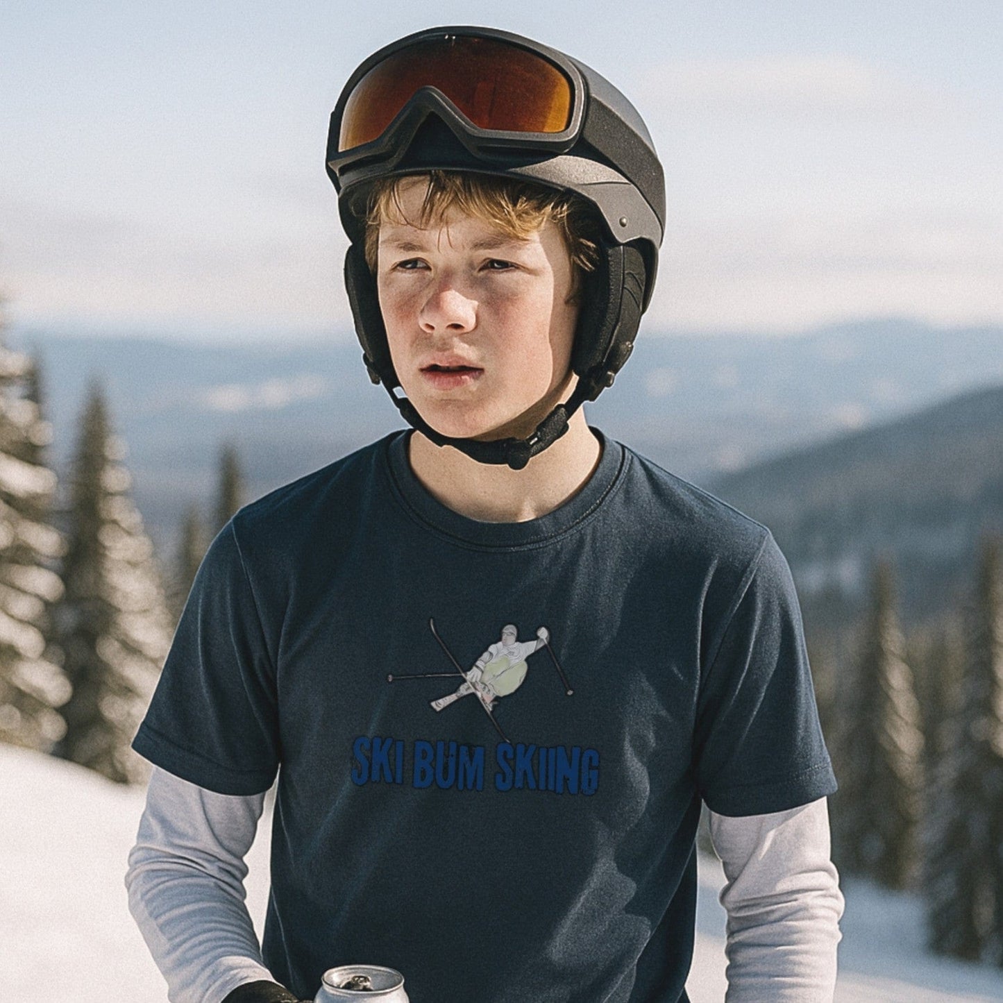 Ski Bum Skiing T-shirt in indigo layered over a base layer, worn on the hill during a sunny mountain break with helmet and drink in hand.