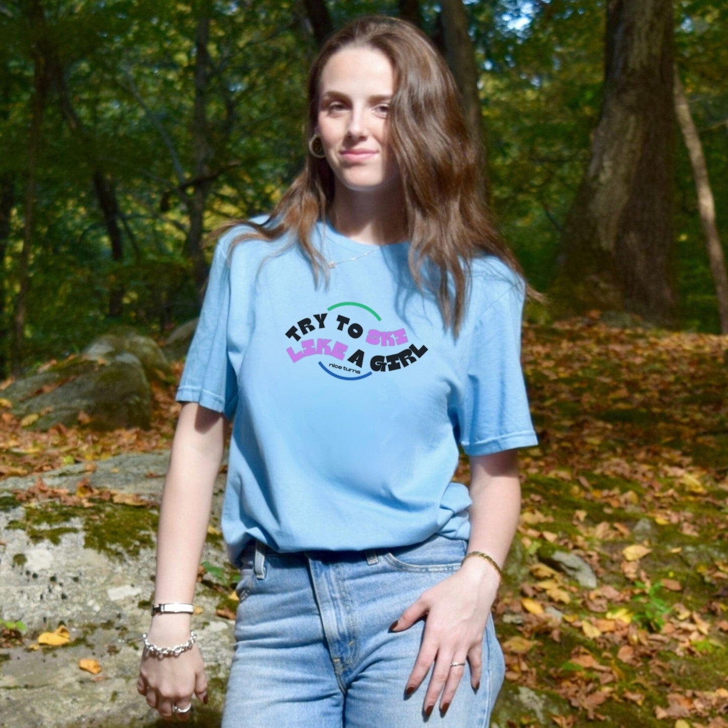 Light blue t-shirt with “Try to Ski Like a Girl” from nice turns, worn casually in a wooded mountain setting on a crisp fall day.