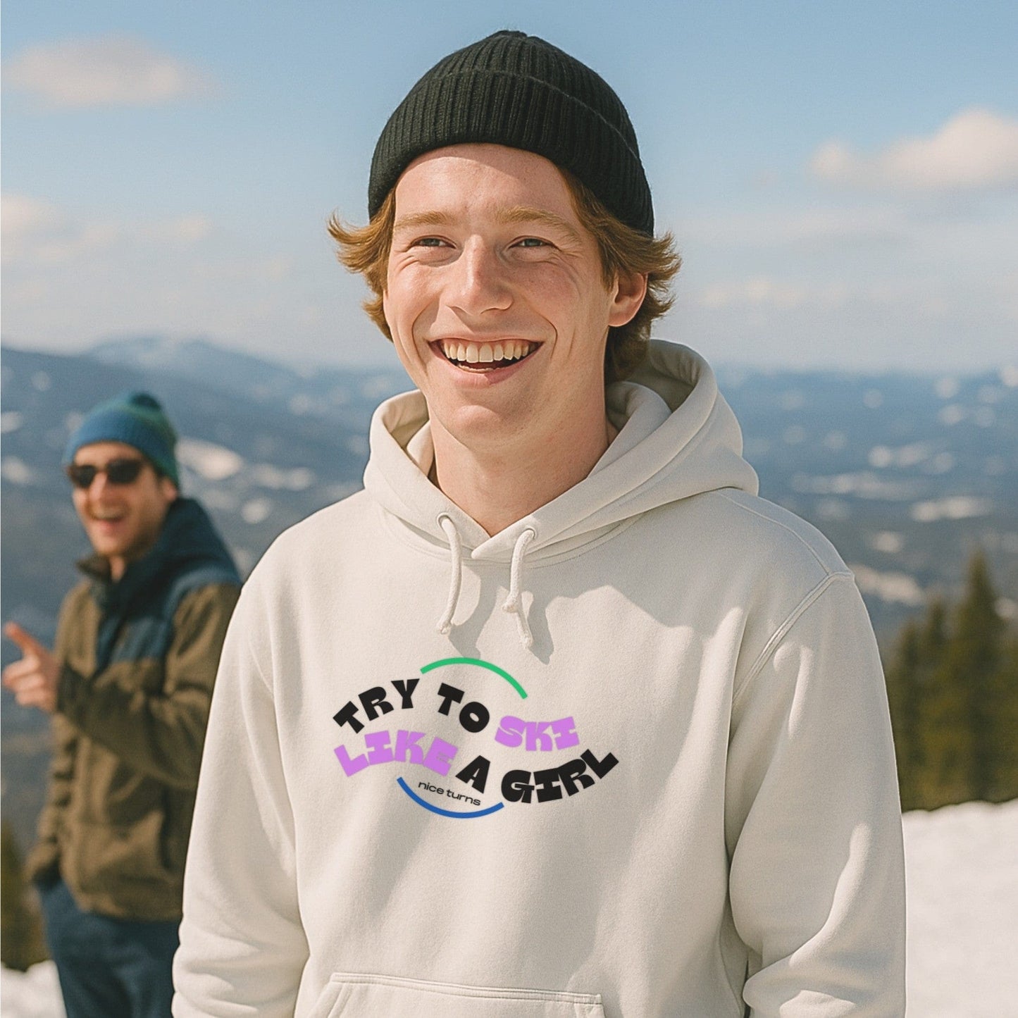 White hoodie with “Try to Ski Like a Girl” design, worn by a smiling skier on a bluebird day with friends at the summit.