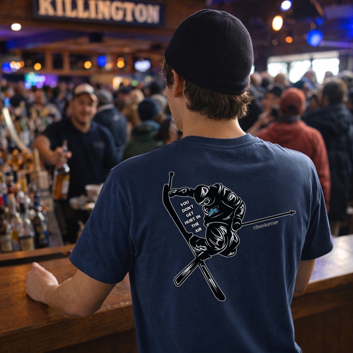 Male skier wearing Indigo t-shirt with back jump graphic in busy bar après setting