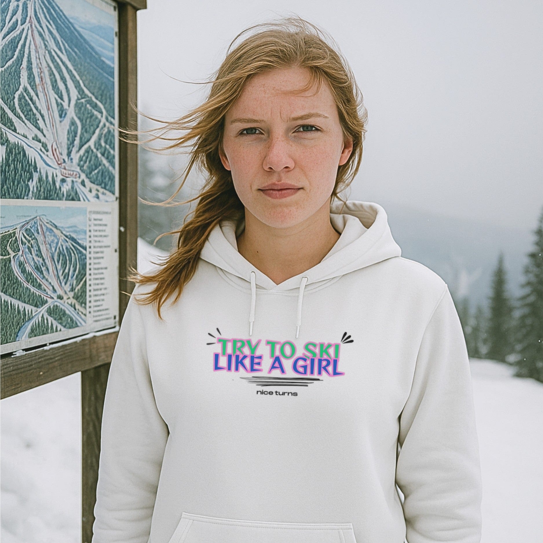 White hoodie with Try to Ski Like a Girl graphic by nice turns, worn near a ski map on a snowy mountain day.