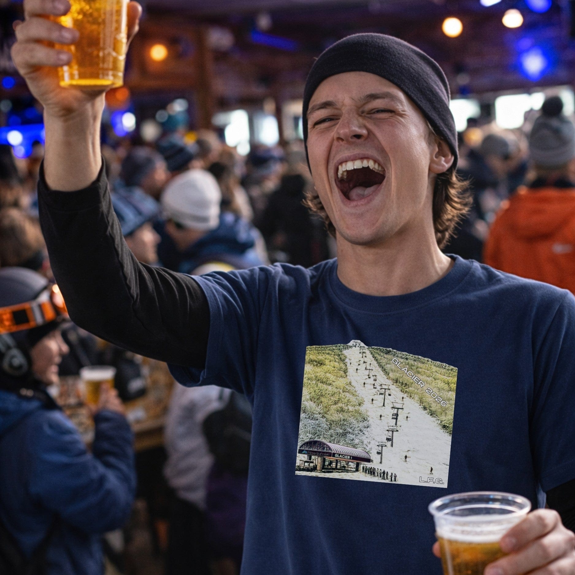 Male skier wearing navy glacier t-shirt front view holding beer at busy bar