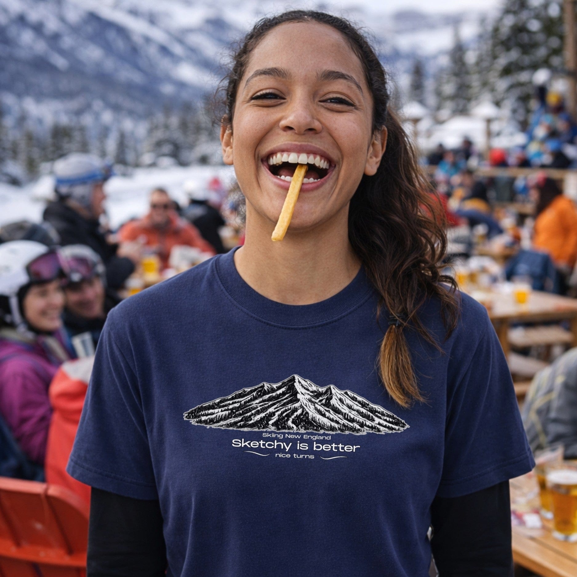 Female skier wearing navy mountain sketch t-shirt eating fries at ski lodge