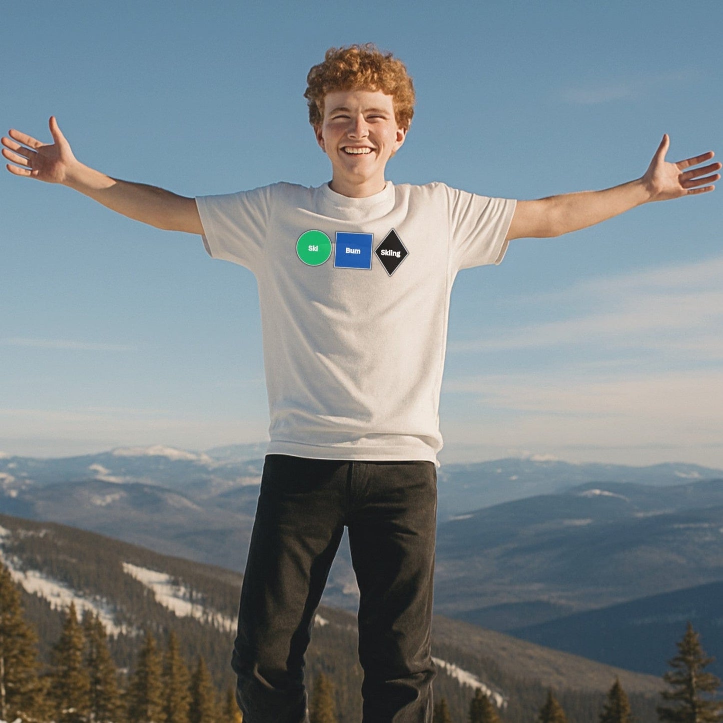A skier spreads his arms wide, smiling at the summit with snowy mountains behind, showing off the white "No Lift Left Behind" tee front graphic.