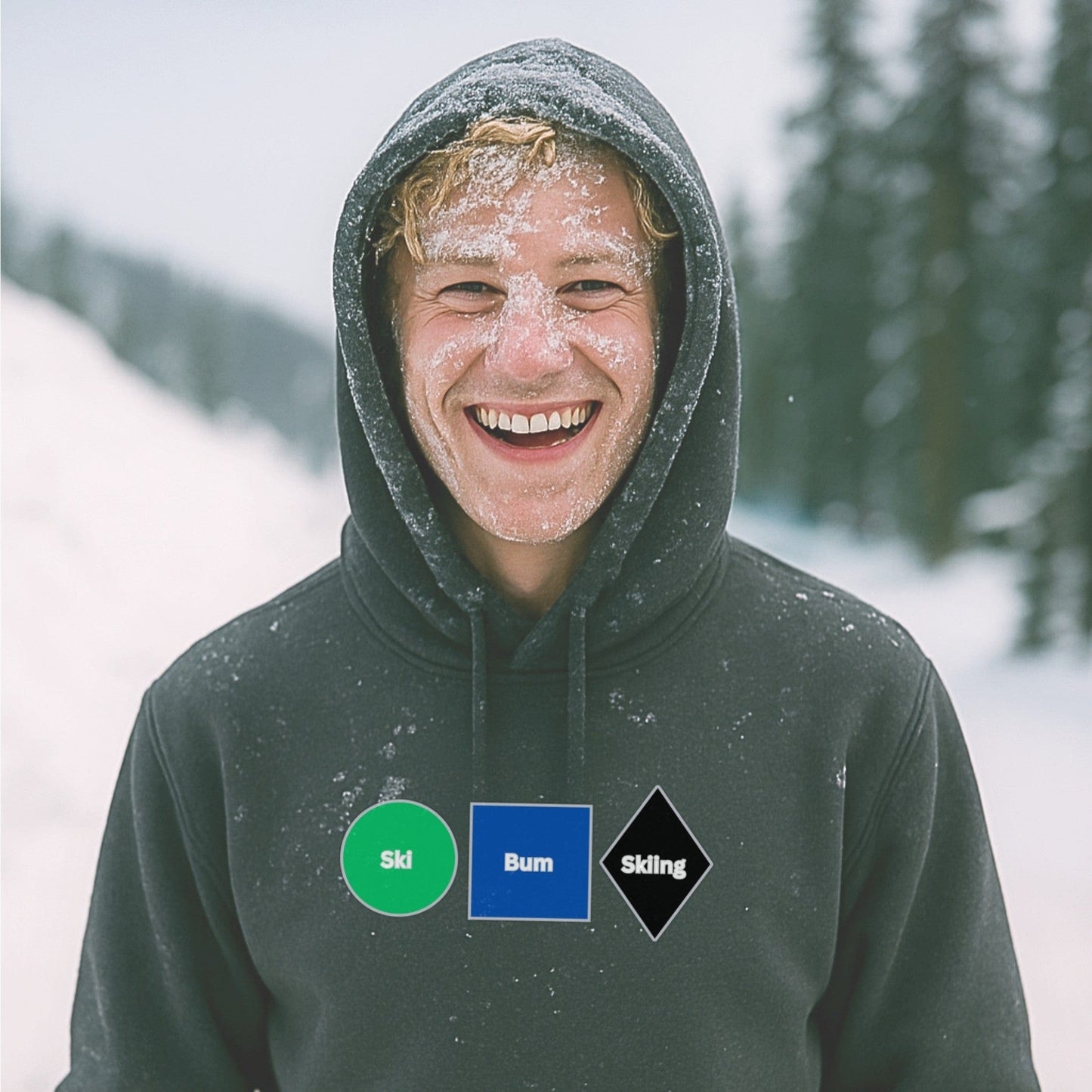 Charcoal hoodie with Ski Bum Skiing design, worn by a snow-covered skier smiling after a powder run on a tree-lined mountain trail.