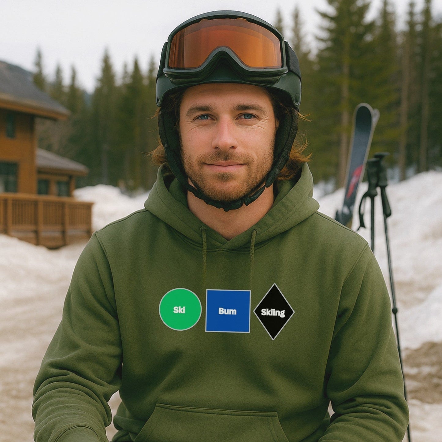 Military green hoodie with Ski Bum Skiing design, worn by a skier relaxing near the lodge with skis and snow-covered trees in the background.