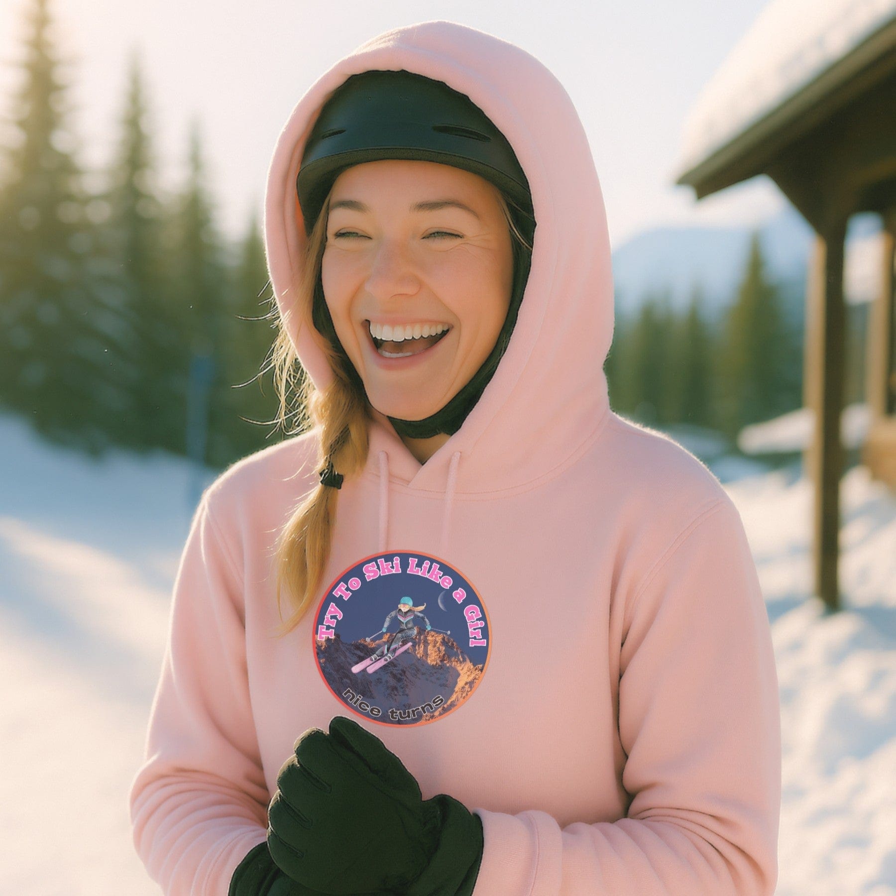 Light pink hoodie with circular Try to Ski Like a Girl design, worn at a sunny ski hill with trees and a lodge in the background.