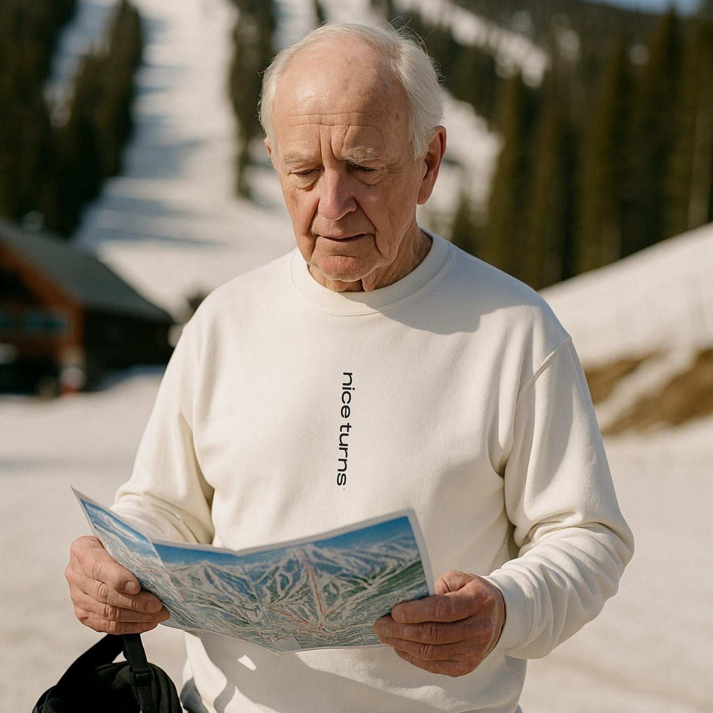 Bashing Bumps Sweatshirt, white, front lifestyle view on spring ski day; skier reading trail map with “nice turns” front mark visible.