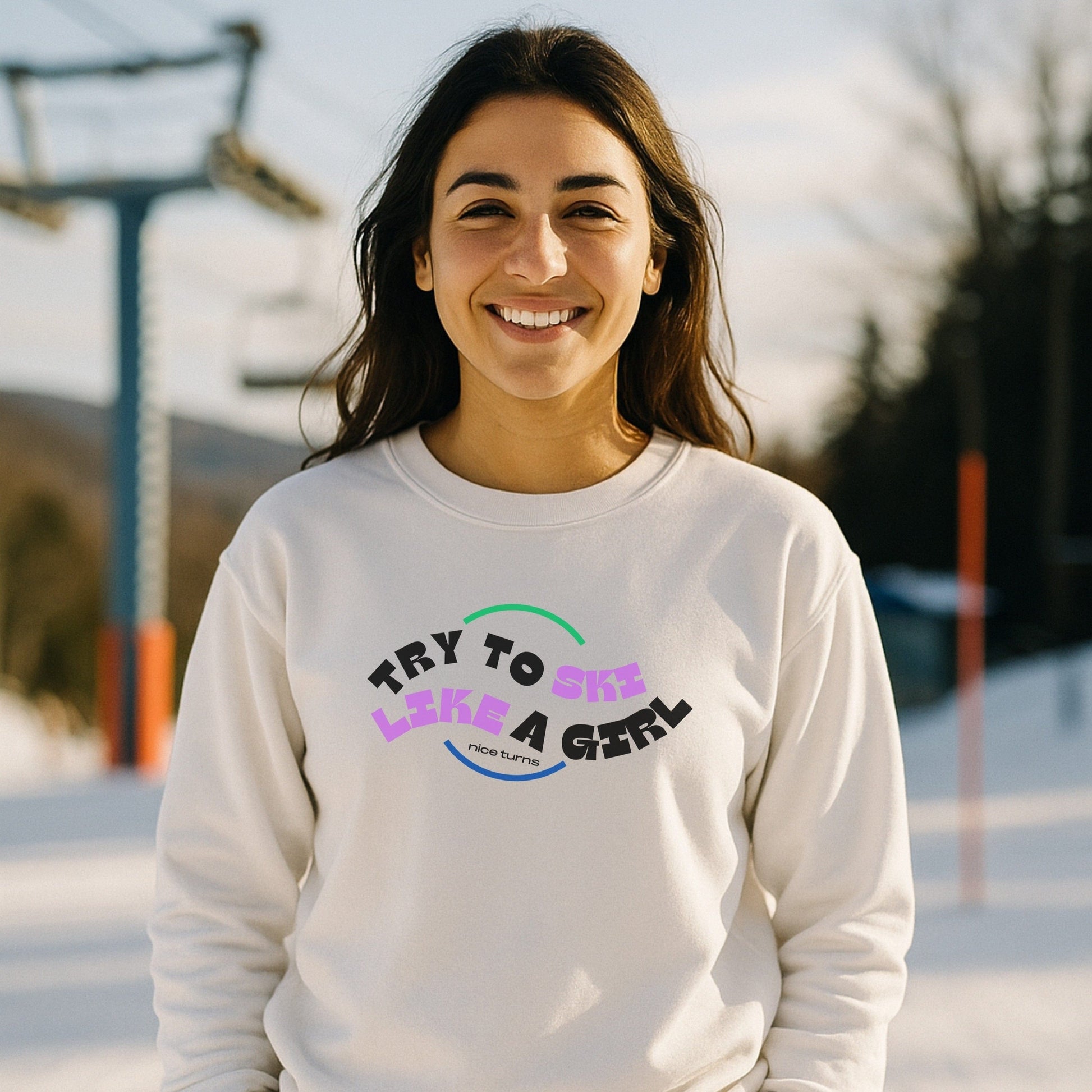 Smiling woman in White “Try to Ski Like a Girl” crewneck at the lift line; clean winter lighting highlights bold retro text and confident skier energy.
