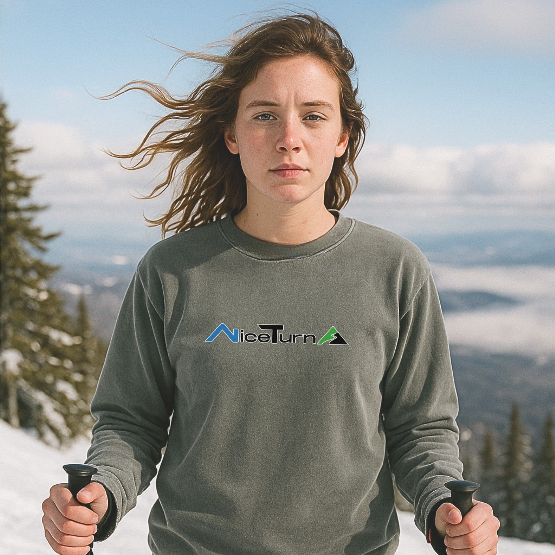Front view of a gray crewneck sweatshirt featuring the nice turns logo, worn by skier holding poles on a bluebird powder day up high.






