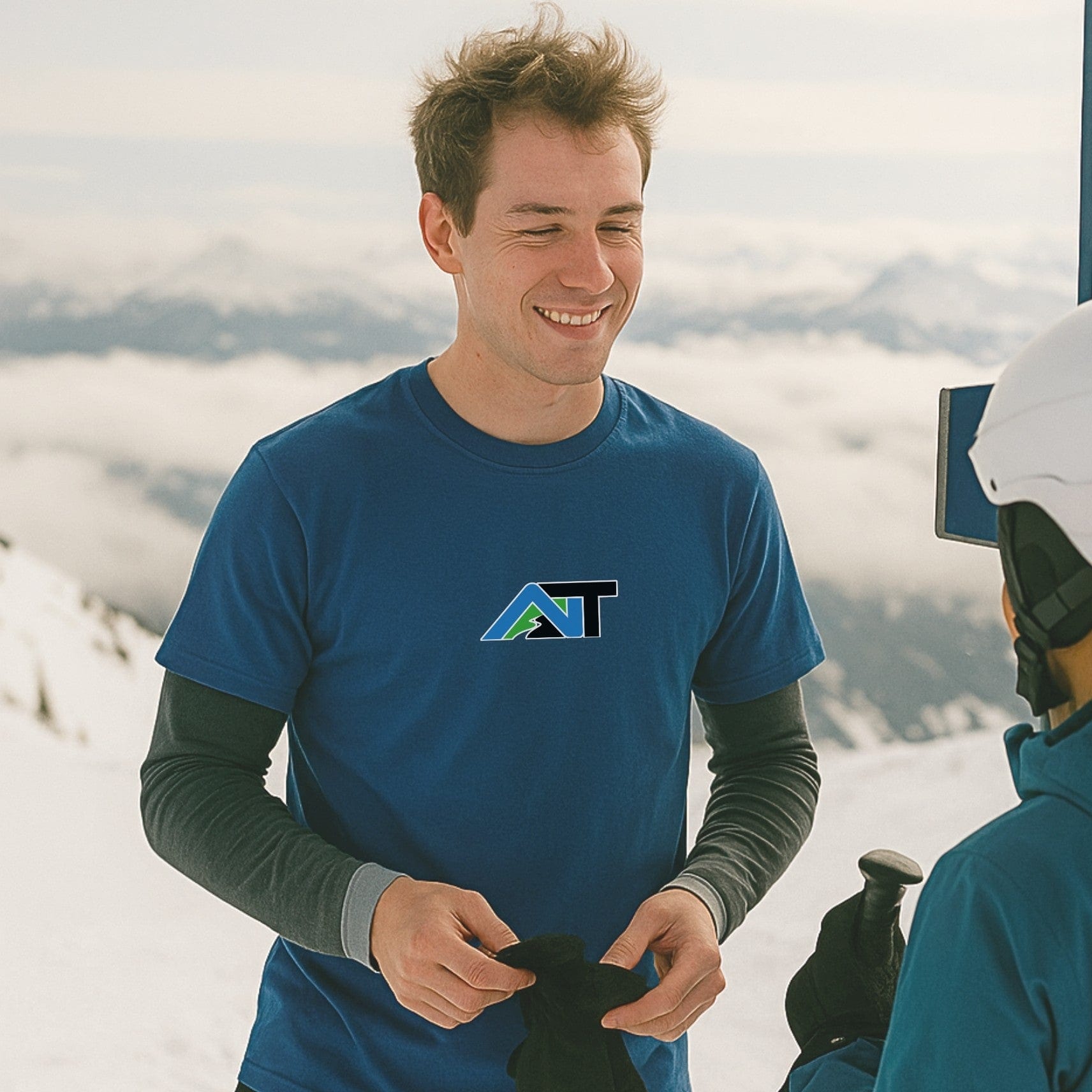Summit Swagger T-shirt in cool blue worn by skier chatting with a friend near a snowy lift station on a cloudy mountaintop.