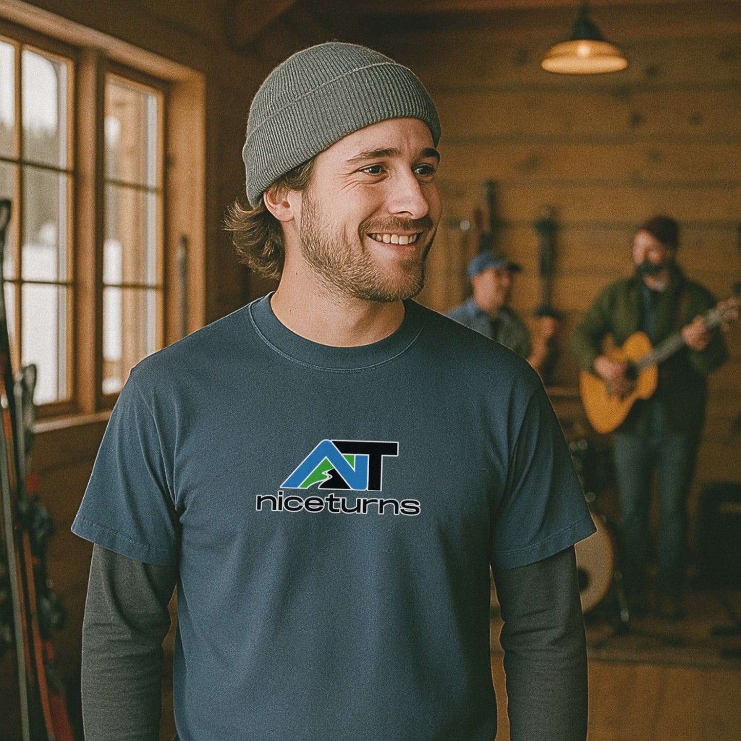Indigo t-shirt with the alpine nice turns logo, worn indoors at a cozy ski lodge with a live band playing in the background.