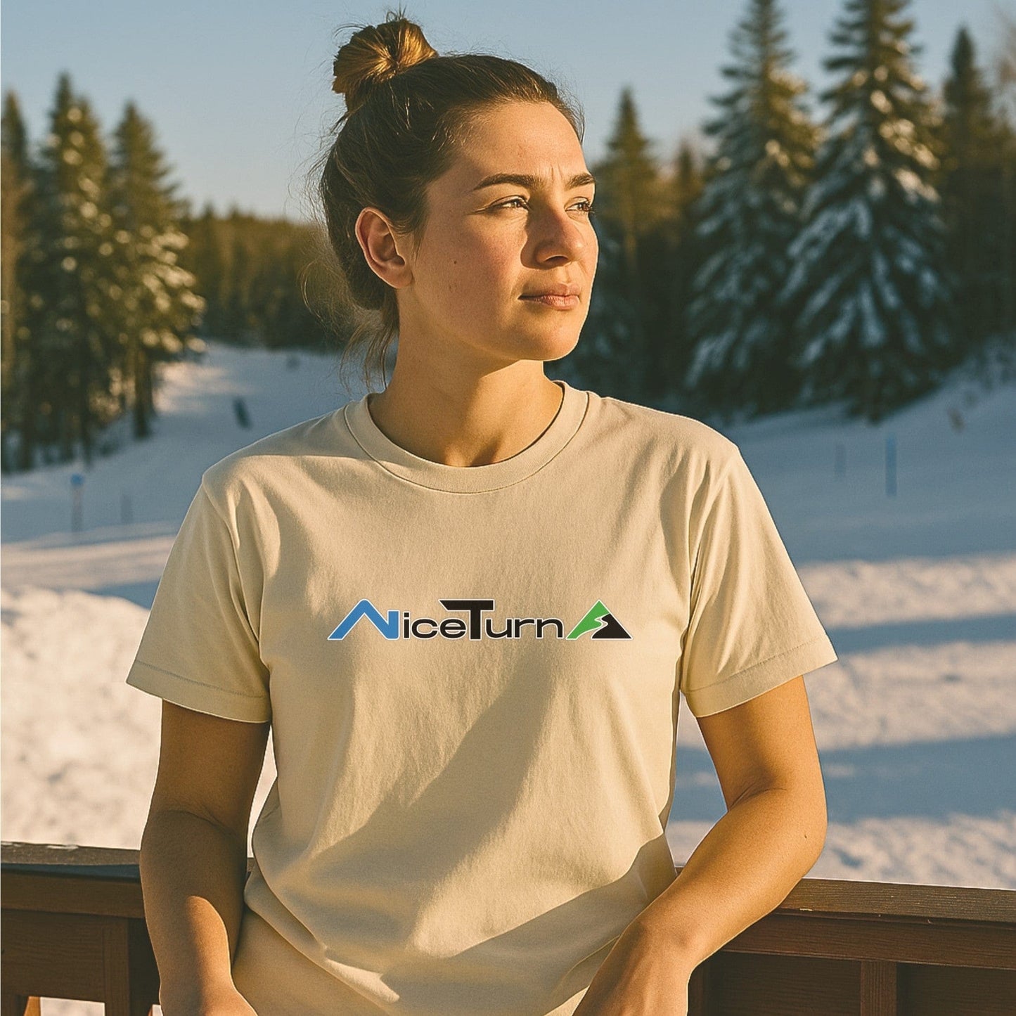Natural-colored short sleeve T-shirt with the Nice Turns logo, worn by a skier at golden hour near a snowy trail and pine trees.