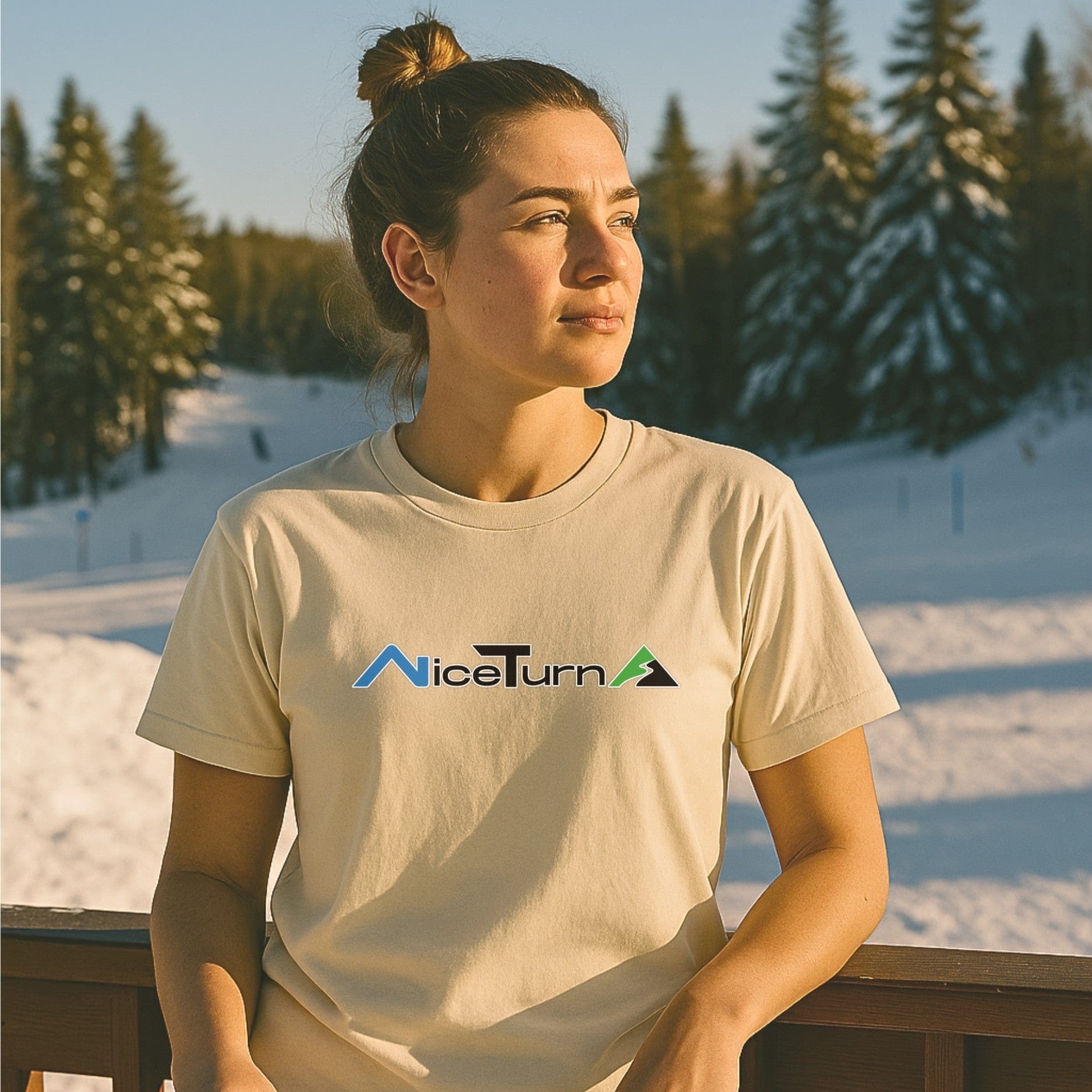 Natural-colored short sleeve T-shirt with the Nice Turns logo, worn by a skier at golden hour near a snowy trail and pine trees.