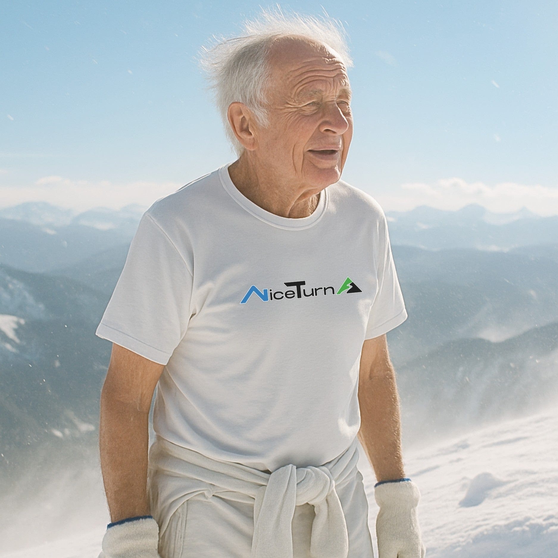 White nice turns logo t-shirt worn by skier on a windy summit with snowy peaks and alpine views stretching across the background.