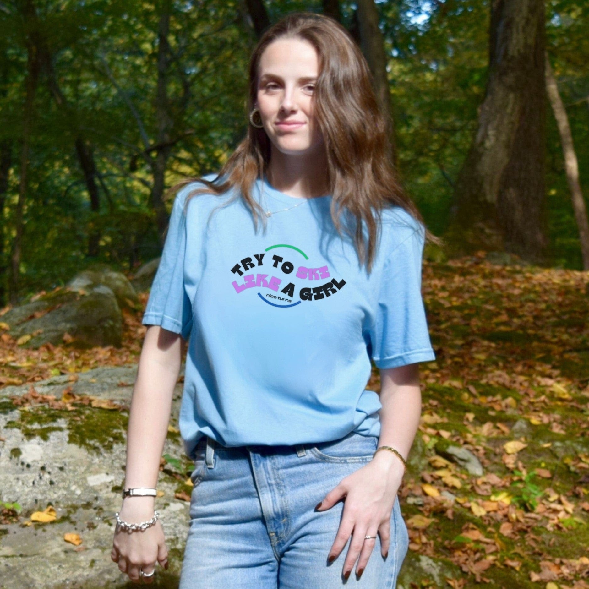 Light blue t-shirt with “Try to Ski Like a Girl” from nice turns, worn casually in a wooded mountain setting on a crisp fall day.