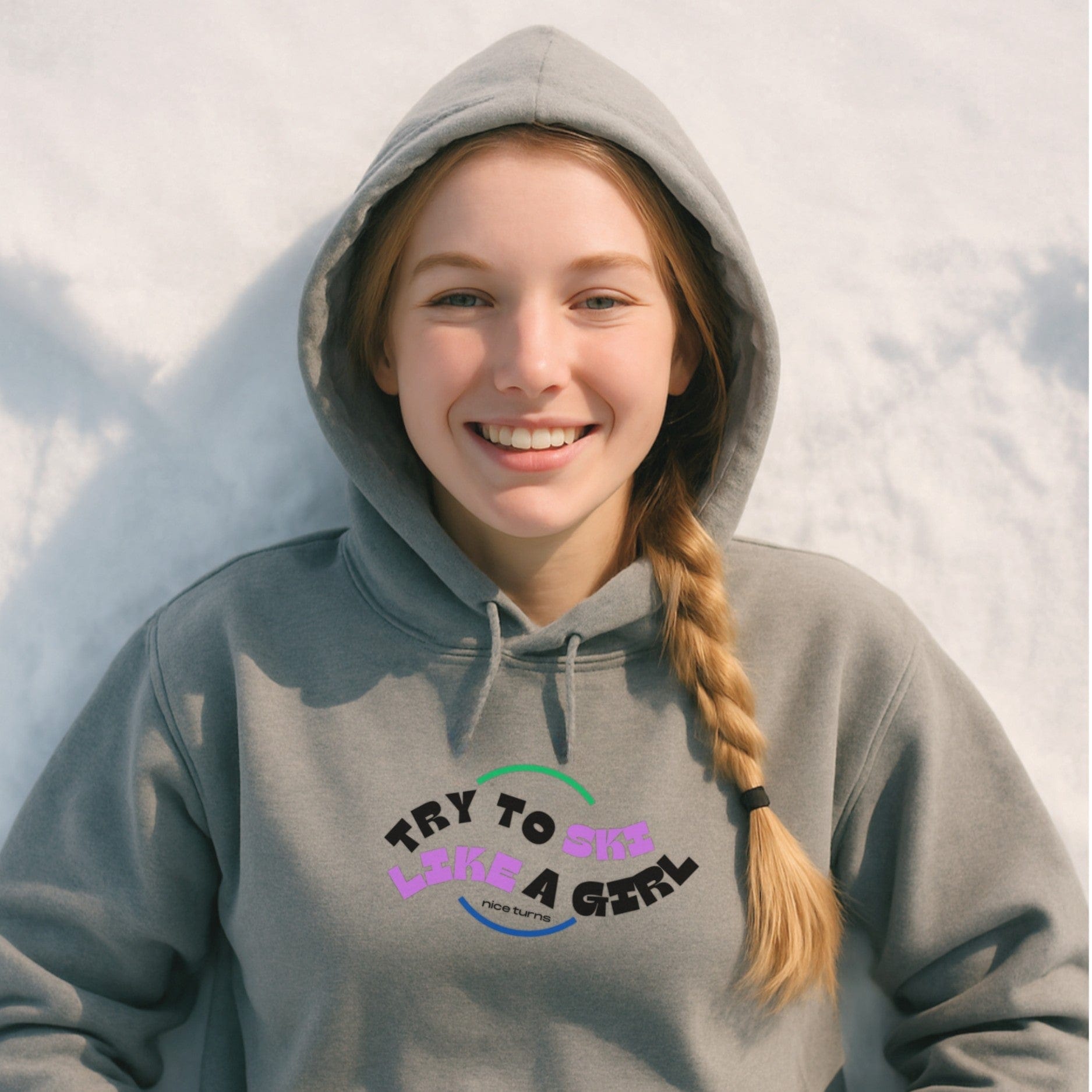 Gray hoodie with “Try to Ski Like a Girl” design, worn by a young skier smiling in the snow after a day on the mountain.