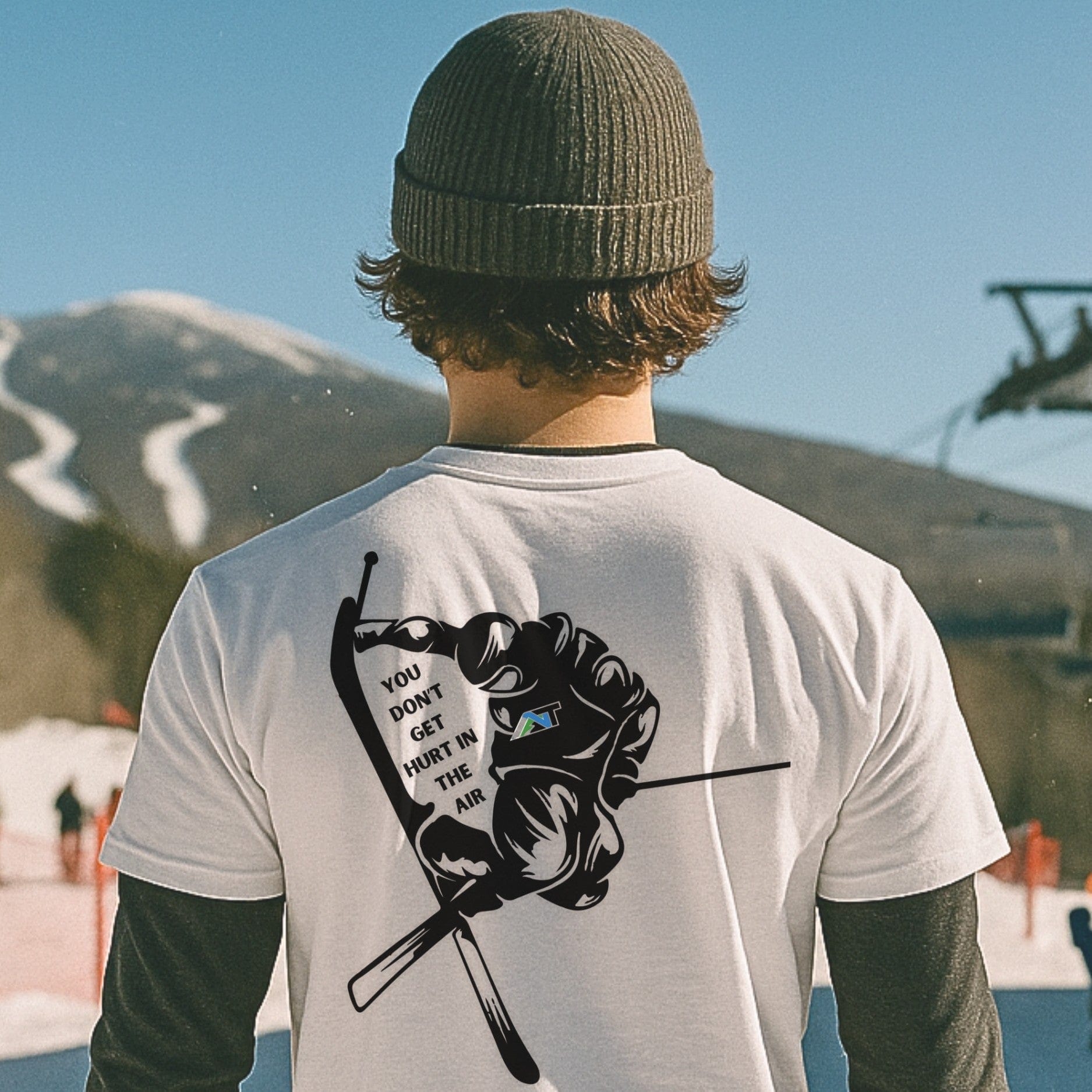 skier in white T-shirt with ski grab graphic standing near lift at base of spring ski mountain